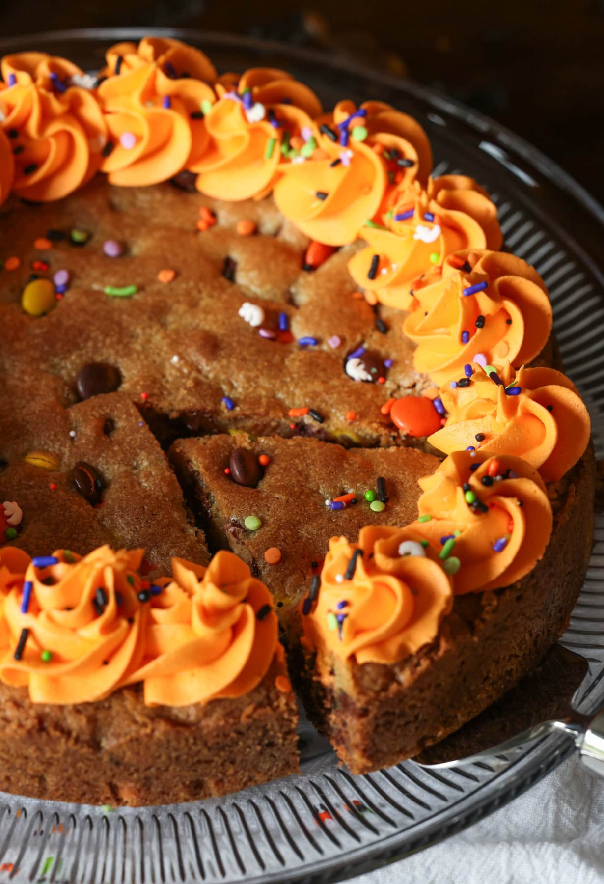 A cookie cake decorated with orange buttercream frosting with a slice being served with a pie serving knife