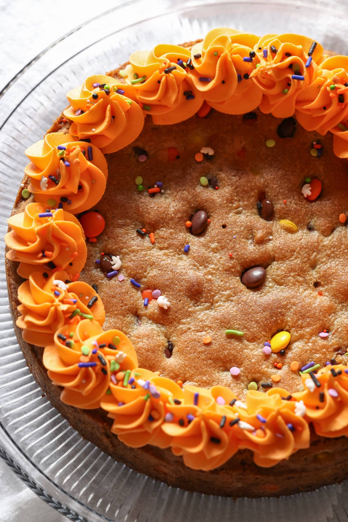 Fluffy orange buttercream frosting swirled around the edge of a biscuit cake