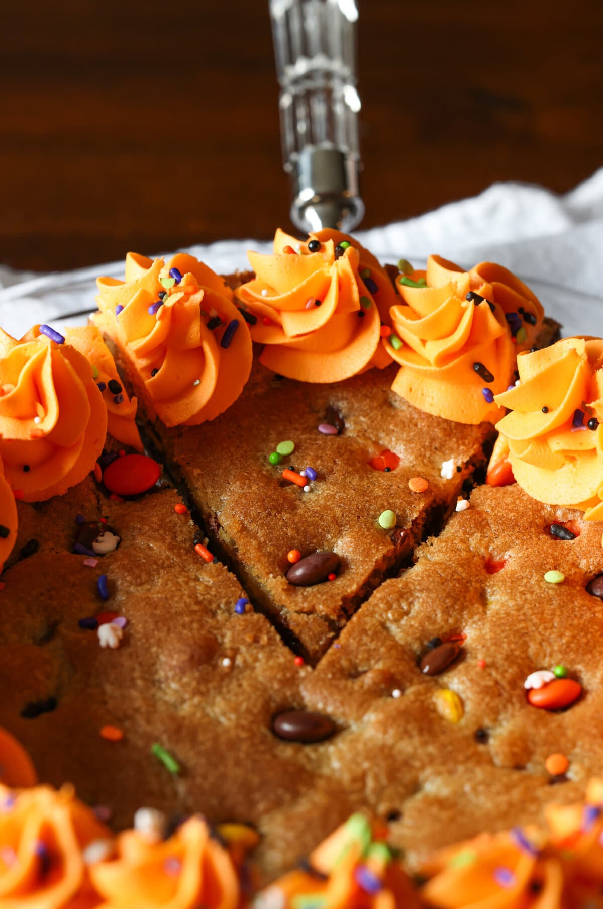 A slice of Halloween cookie cake with orange frosting being cut and served with a spatula.