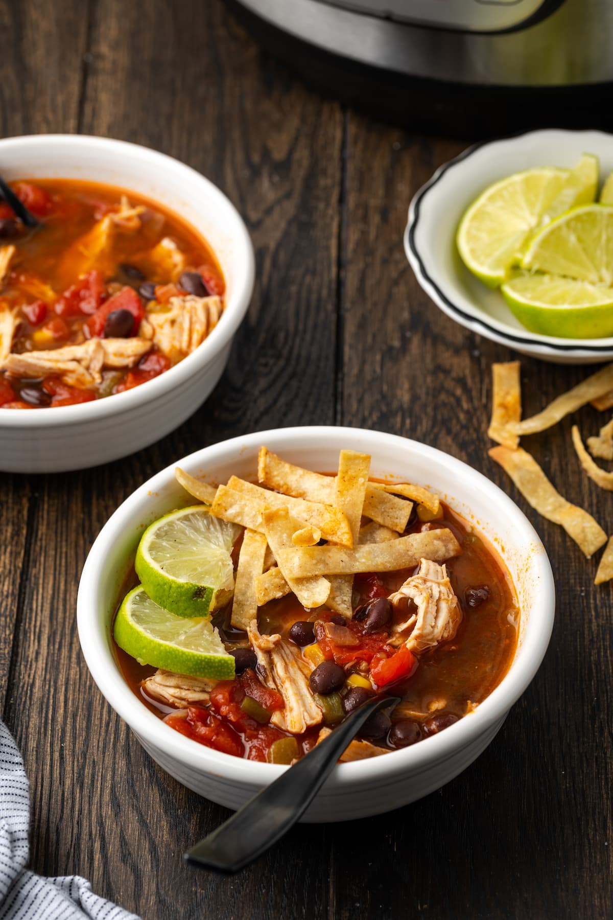 A bowl of chicken tortilla soup garnished with lime wedges and crispy tortilla strips, with a bowl of lime wedges in the background.