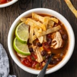 Overhead view of a bowl of chicken tortilla soup garnished with lime wedges and crispy tortilla strips.