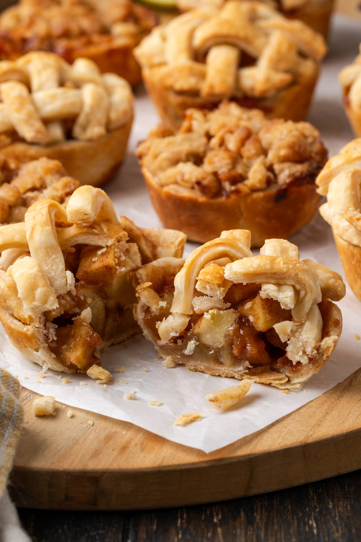 Mini apple pies on a piece of parchment paper, with one pie cut in half to reveal the apple pie filling.