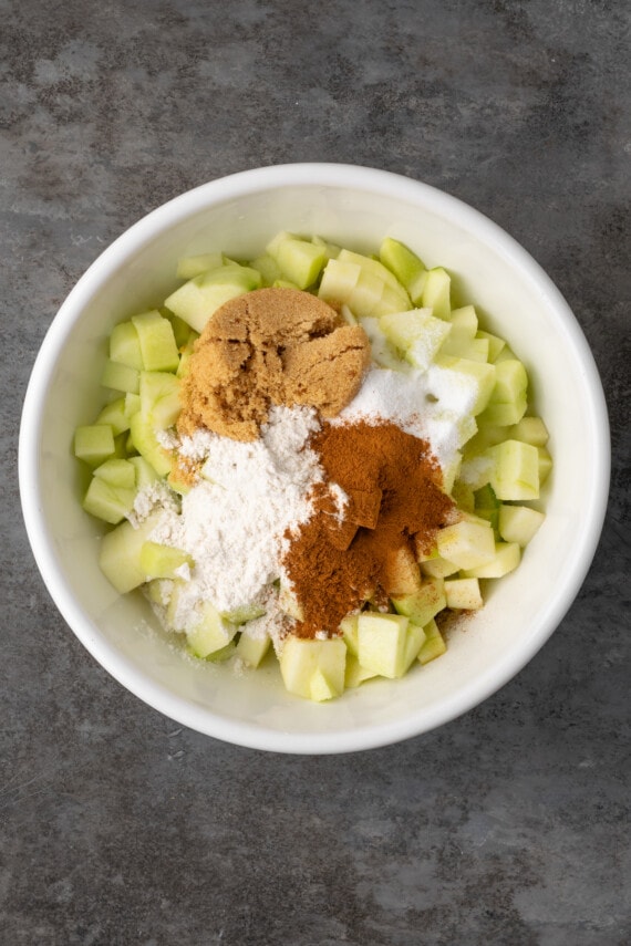 Apple pie filling ingredients added to a bowl of chopped apples.