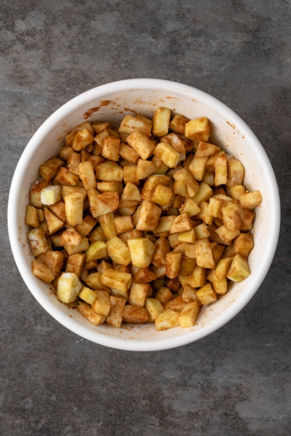 Chopped apples coated in sugar and spices in a large bowl.