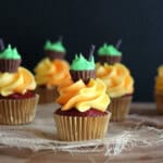 A mini halloween cupcake frosted with orange frosting and topped with a mini peanut butter cup and green icing meant to look like a cauldron
