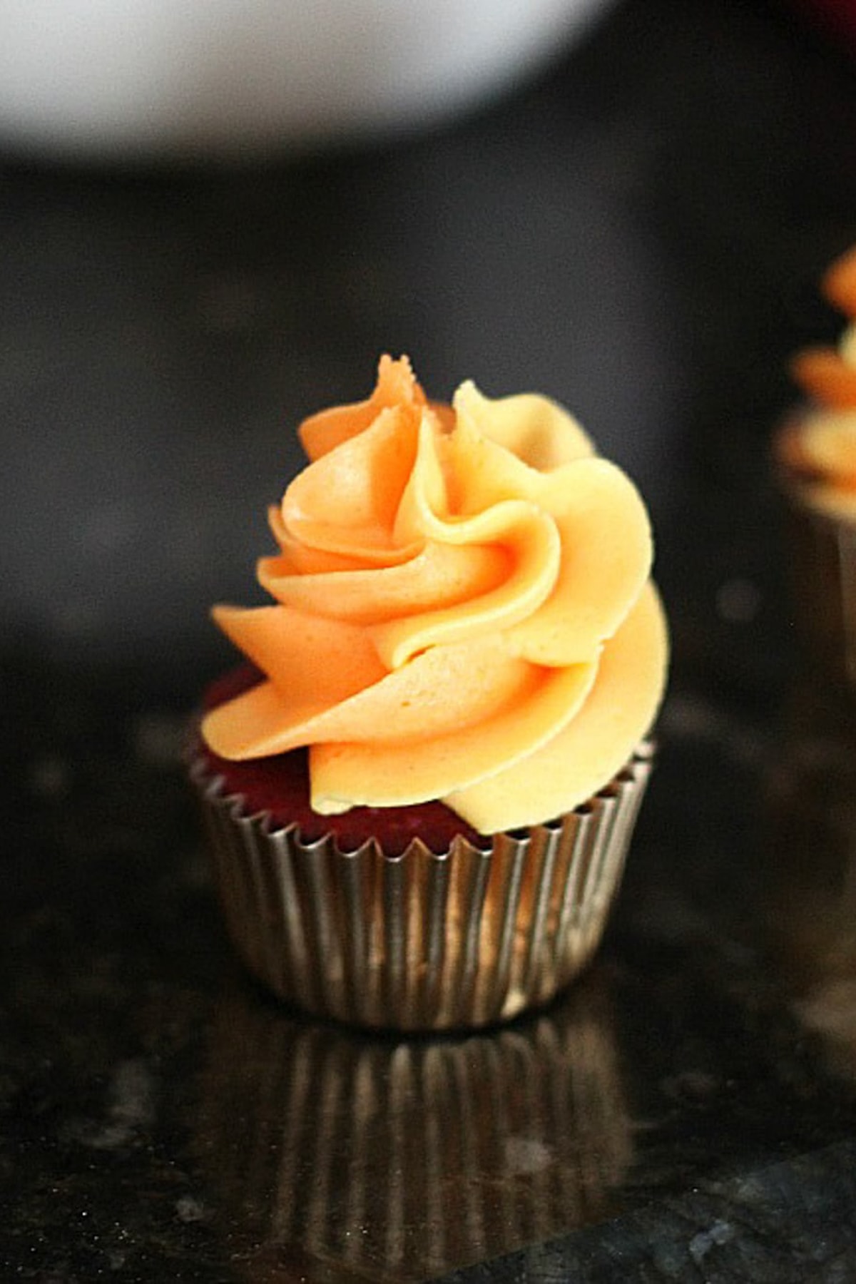 A mini cupcake topped with a swirl of orange frosting.