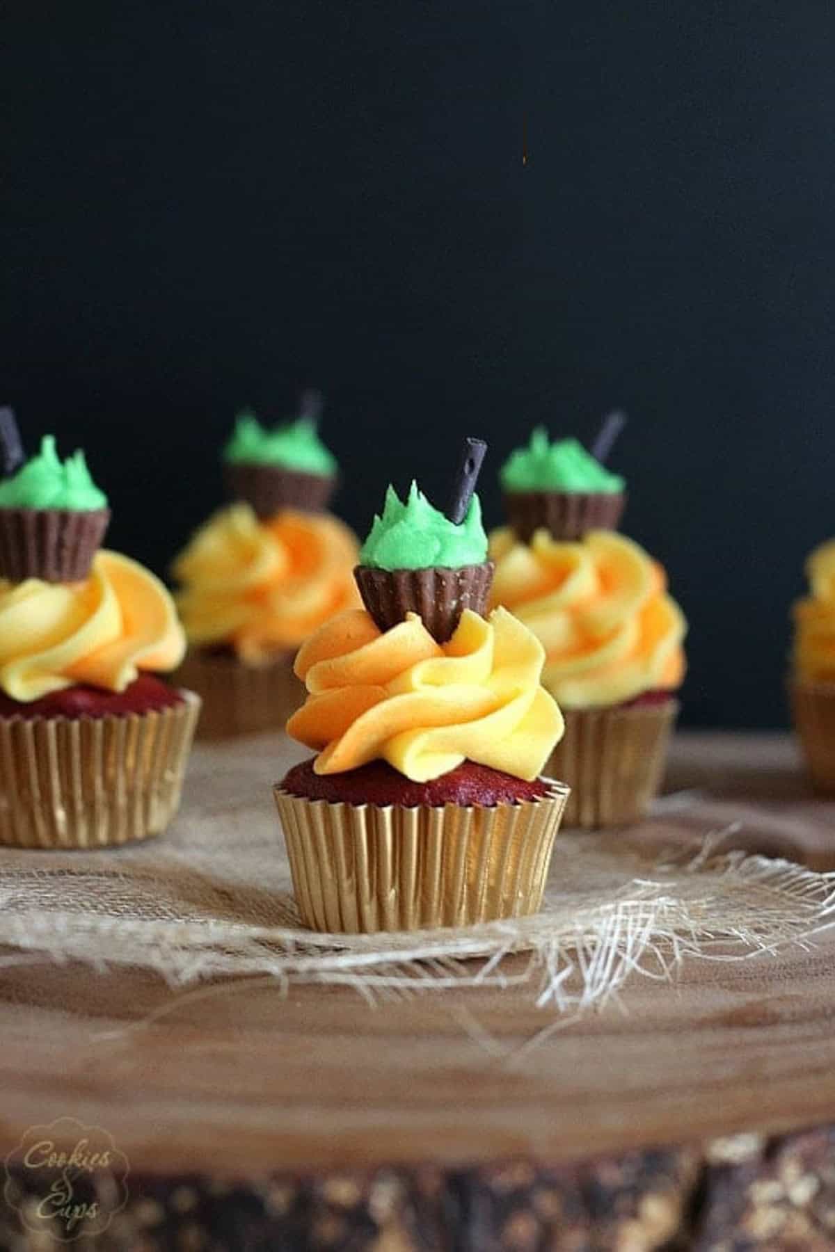 A mini halloween cupcake frosted with orange frosting and topped with a mini peanut butter cup and green icing meant to look like a cauldron
