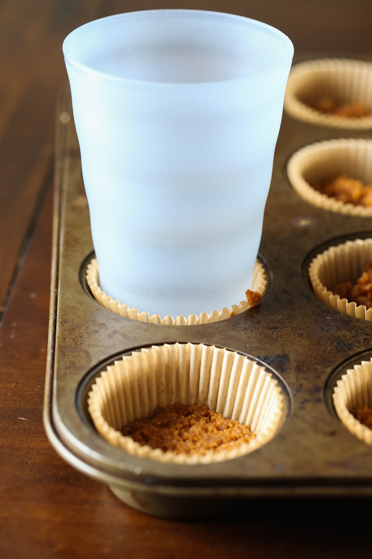 Pressing crust mixture into muffin liners with a cup.