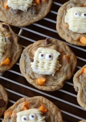 A white chocolate covered pretzel decorated like a mummy on top of a chocolate chip cookie