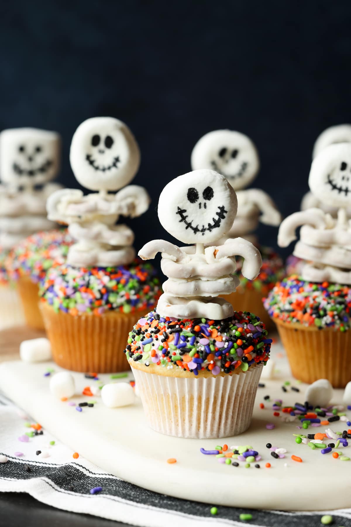 Skeletons with marshmallow heads and white chocolate pretzel "rib cages" on top of sprinkle covered cupcakes