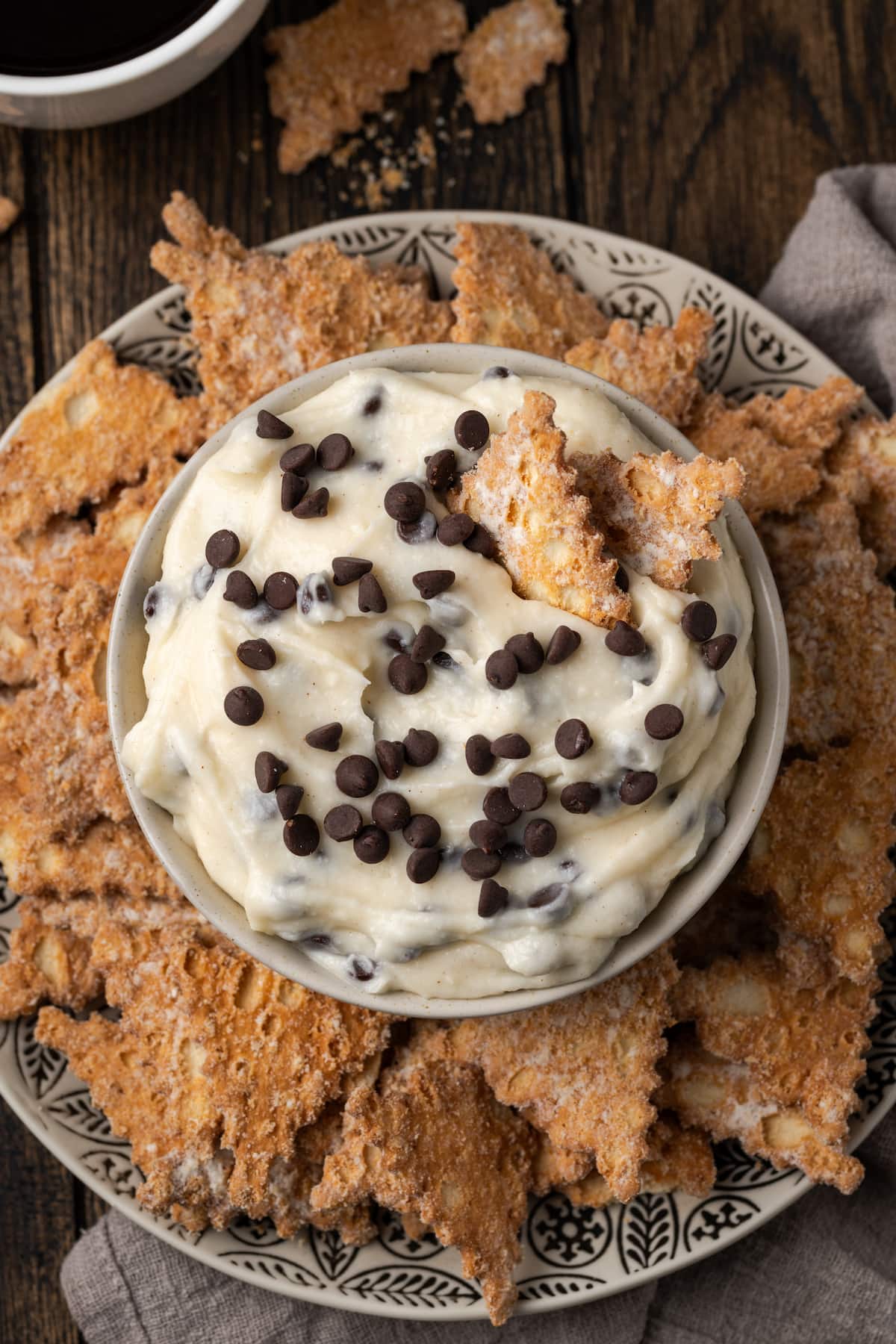 Overhead view of cannoli dip served in a bowl, surrounded by cookies on a plate.