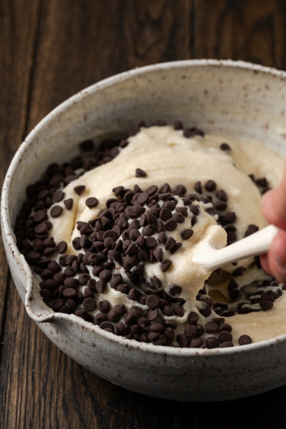 Chocolate chips are folded into cannoli dip in a large bowl.