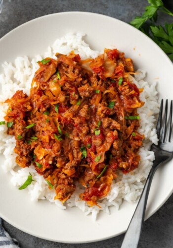 Overhead view of unstuffed cabbage served over rice on a white plate next to a fork.