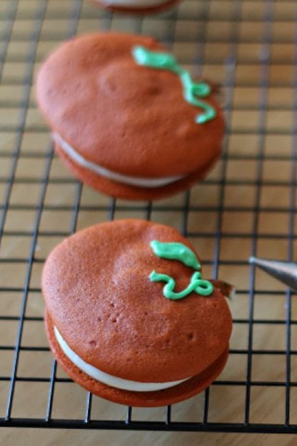 Green icing piped onto an orange sandwich cookie to look like a pumpkin vine.