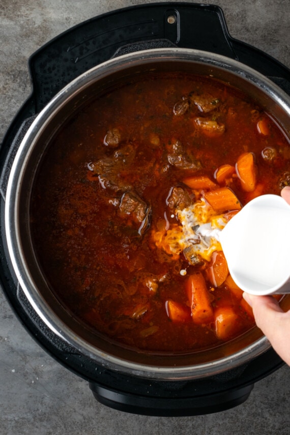 A slurry of tapioca starch and water is poured into the beef stew inside the instant pot.