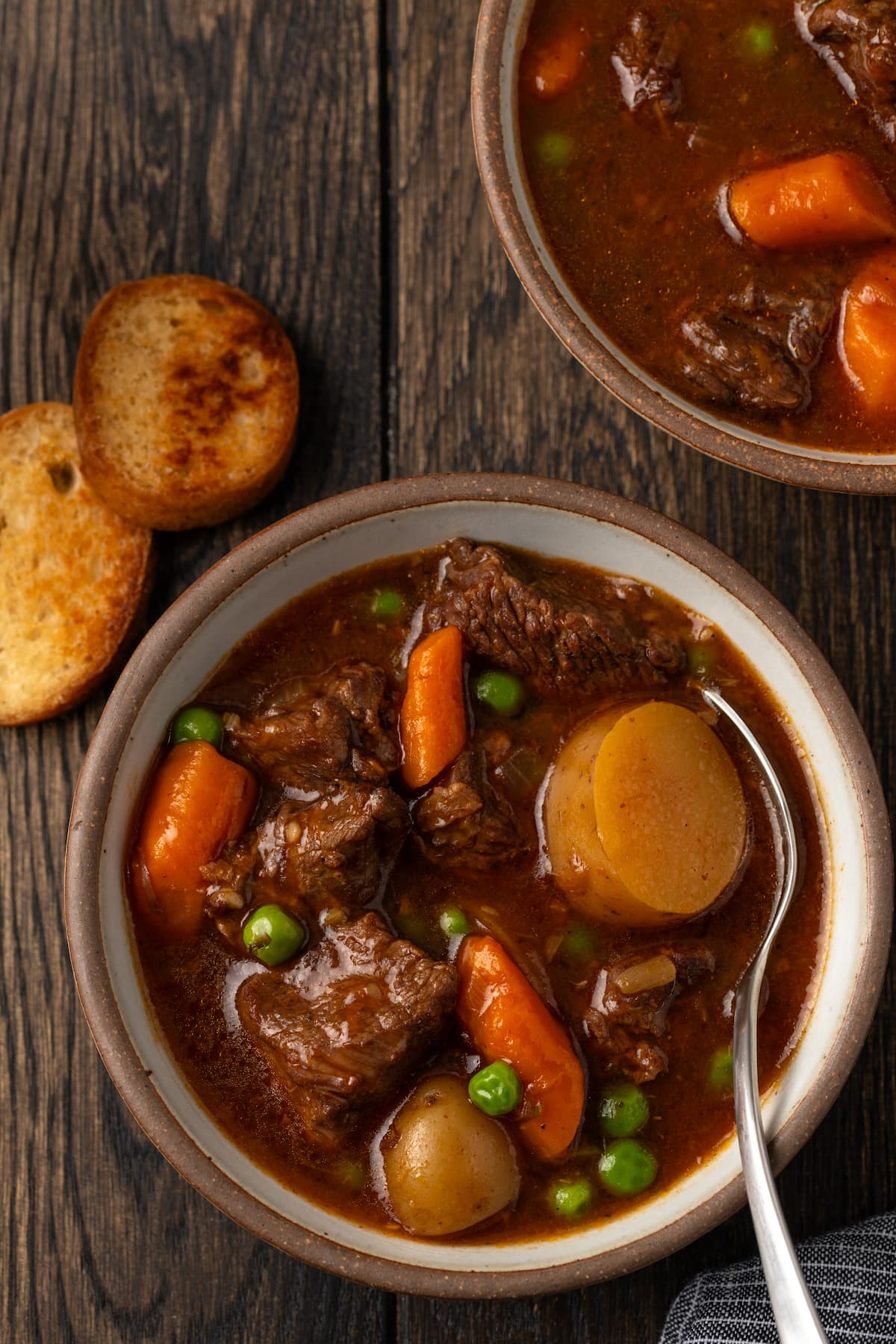 Overhead view of a bowl of Instant Pot beef stew on a wooden table, next to a second bowl and crostini.