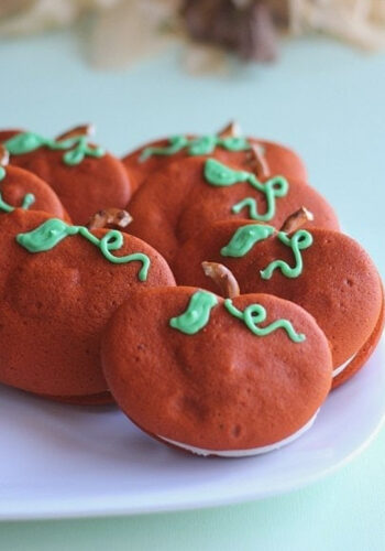Pumpkin Whoopie Pies with pretzel stems and green frosted vines on a white plate