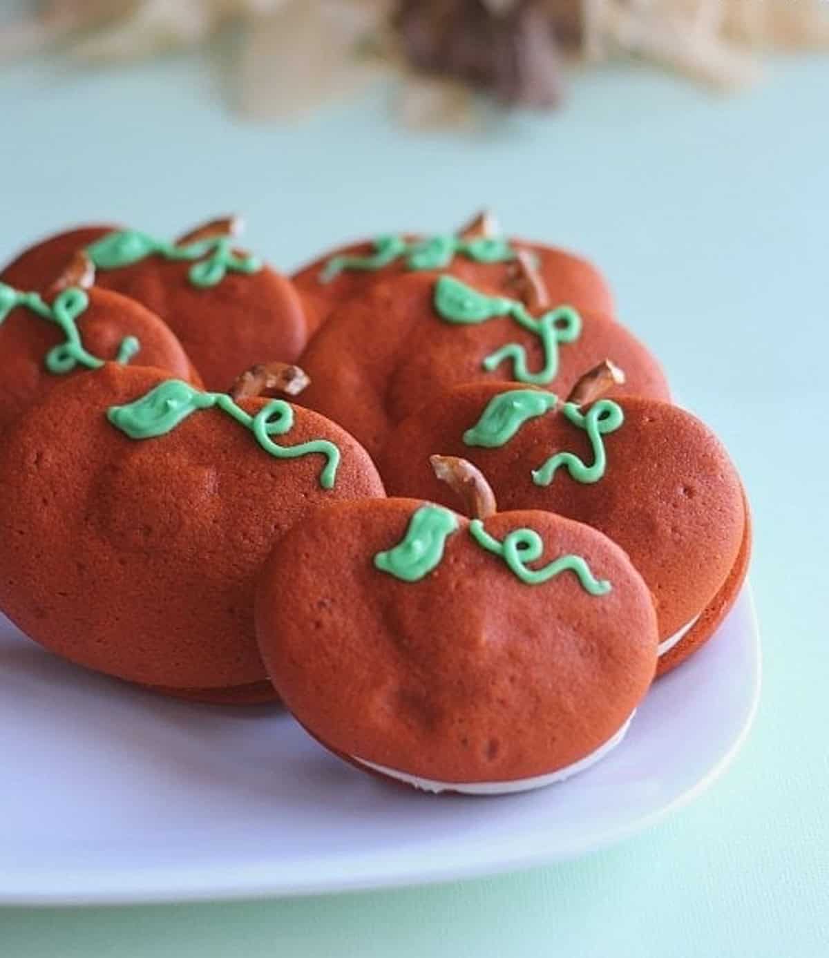 Pumpkin Whoopie Pies with pretzel stems and green frosted vines on a white plate