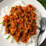 Overhead view of unstuffed cabbage served over rice on a white plate next to a fork.