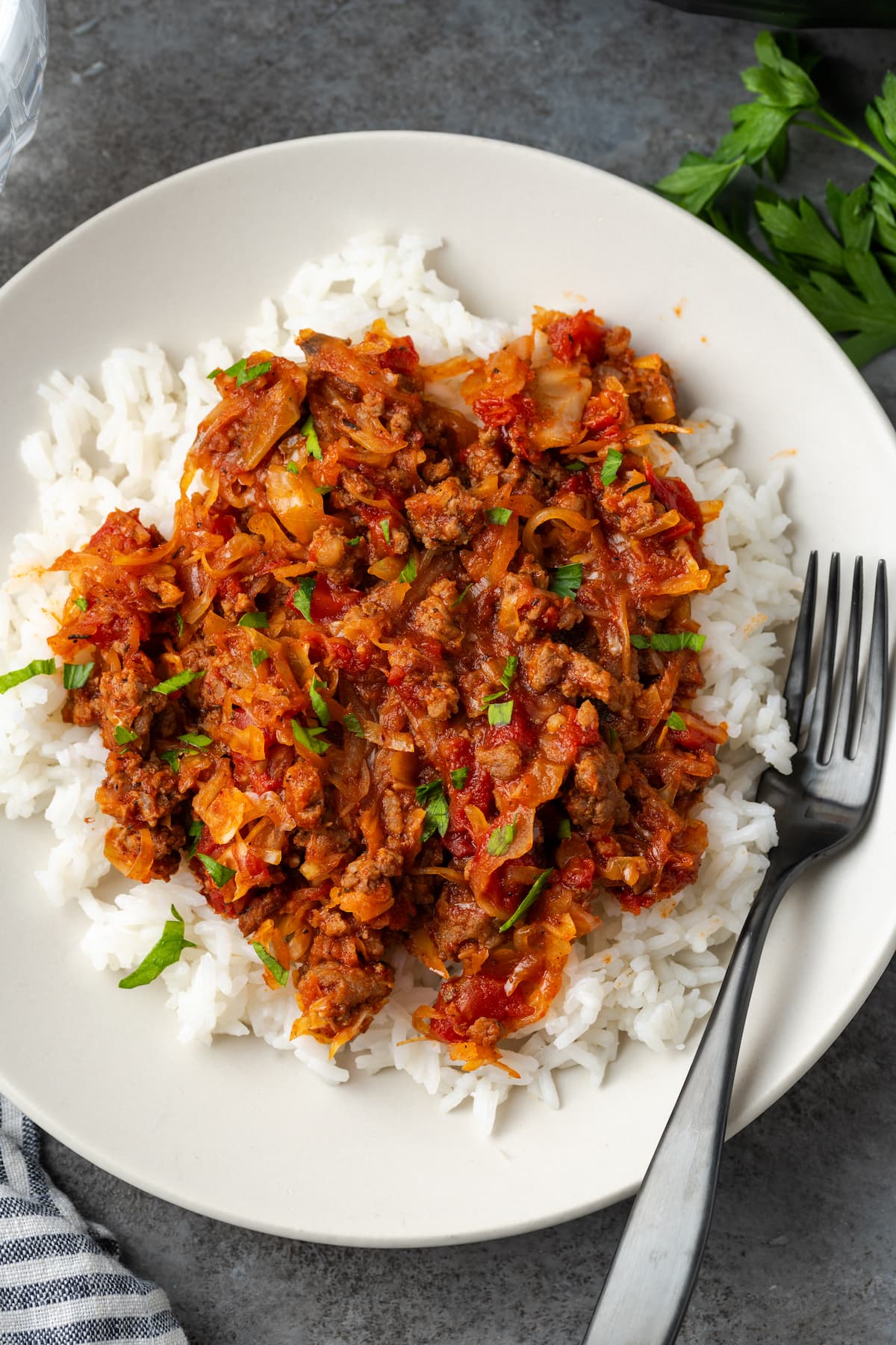 Overhead view of unstuffed cabbage served over rice on a white plate next to a fork.