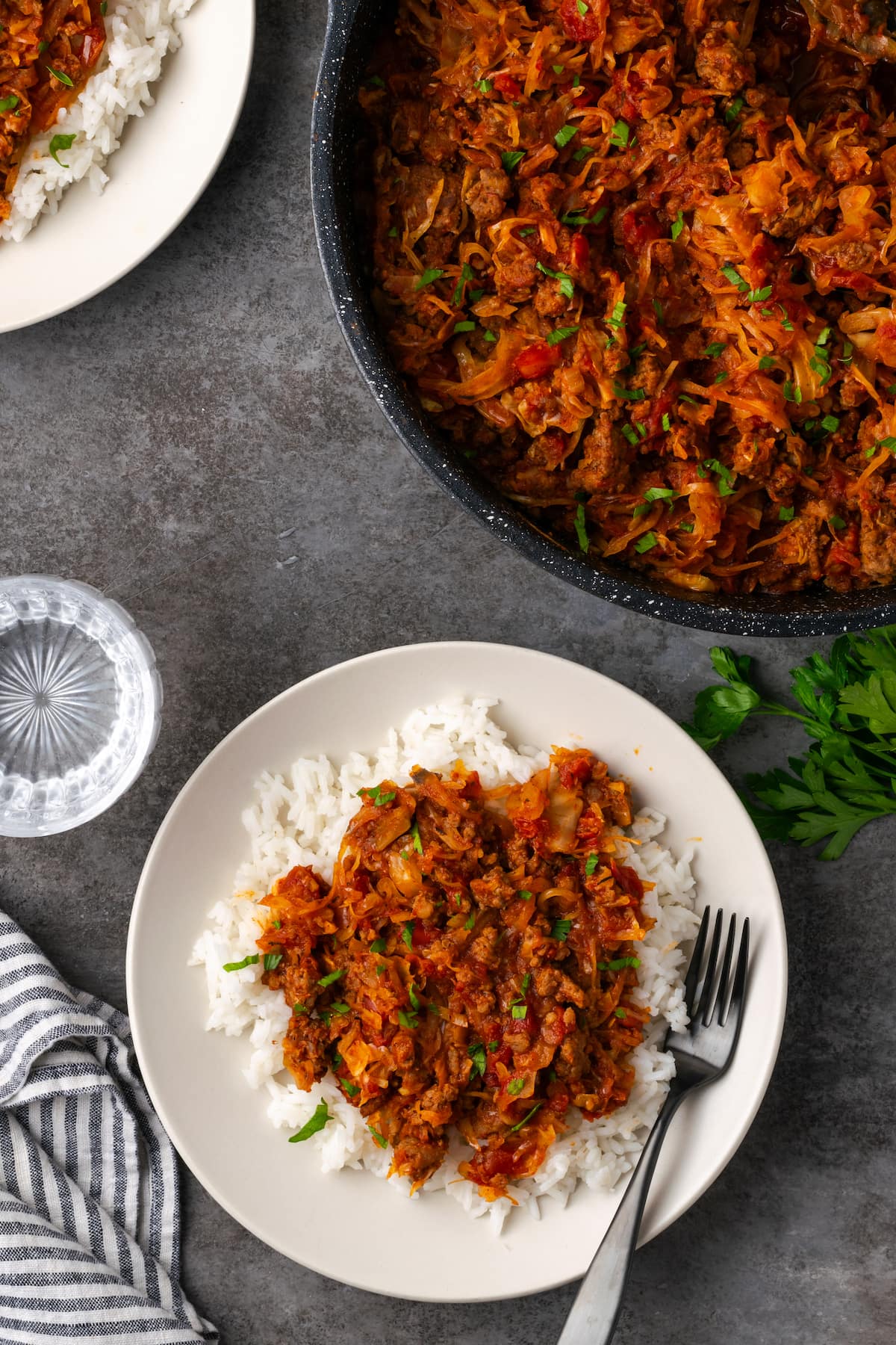 Overhead view of unstuffed cabbage served over rice on a white plate next to more cabbage in a large pot.