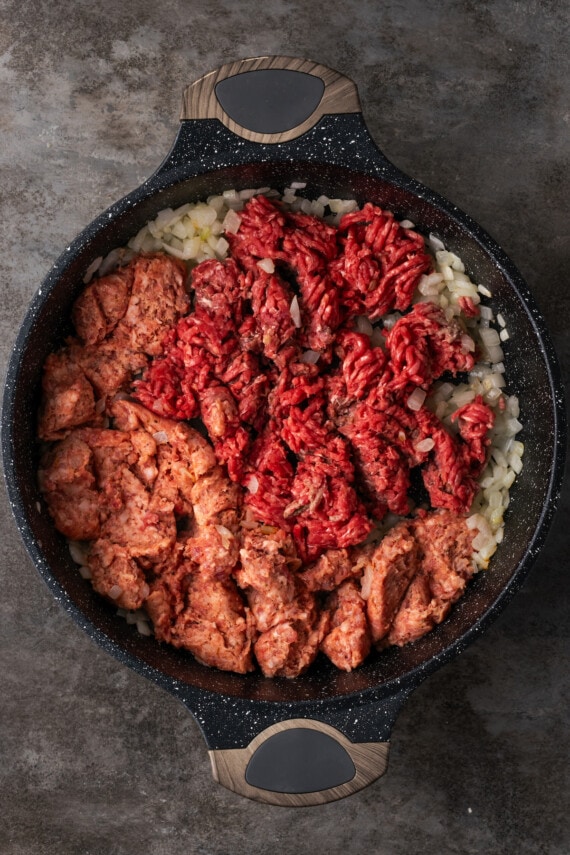 Ground beef and pork sausage added to diced onion in a skillet.