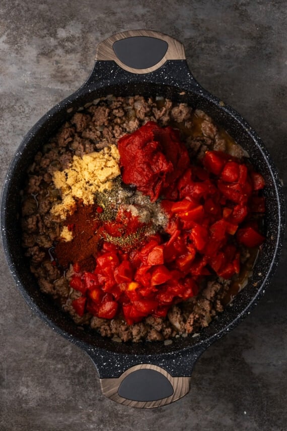 Tomatoes, tomato paste, and seasonings added to browned ground beef in a skillet.