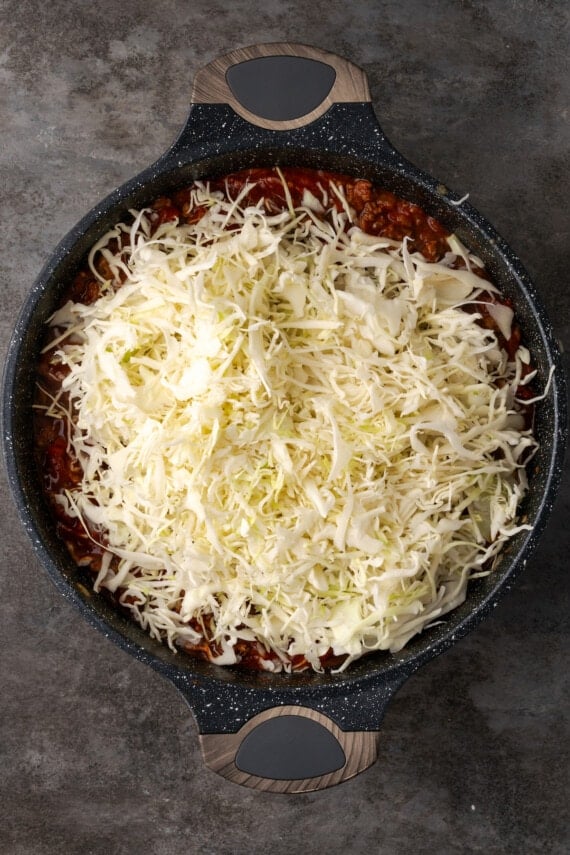 Shredded cabbage added to a skillet with ground beef and tomatoes.