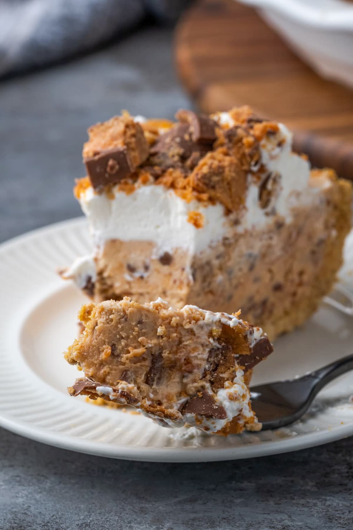 A forkful of Butterfinger pie on a white plate next to a pie slice.
