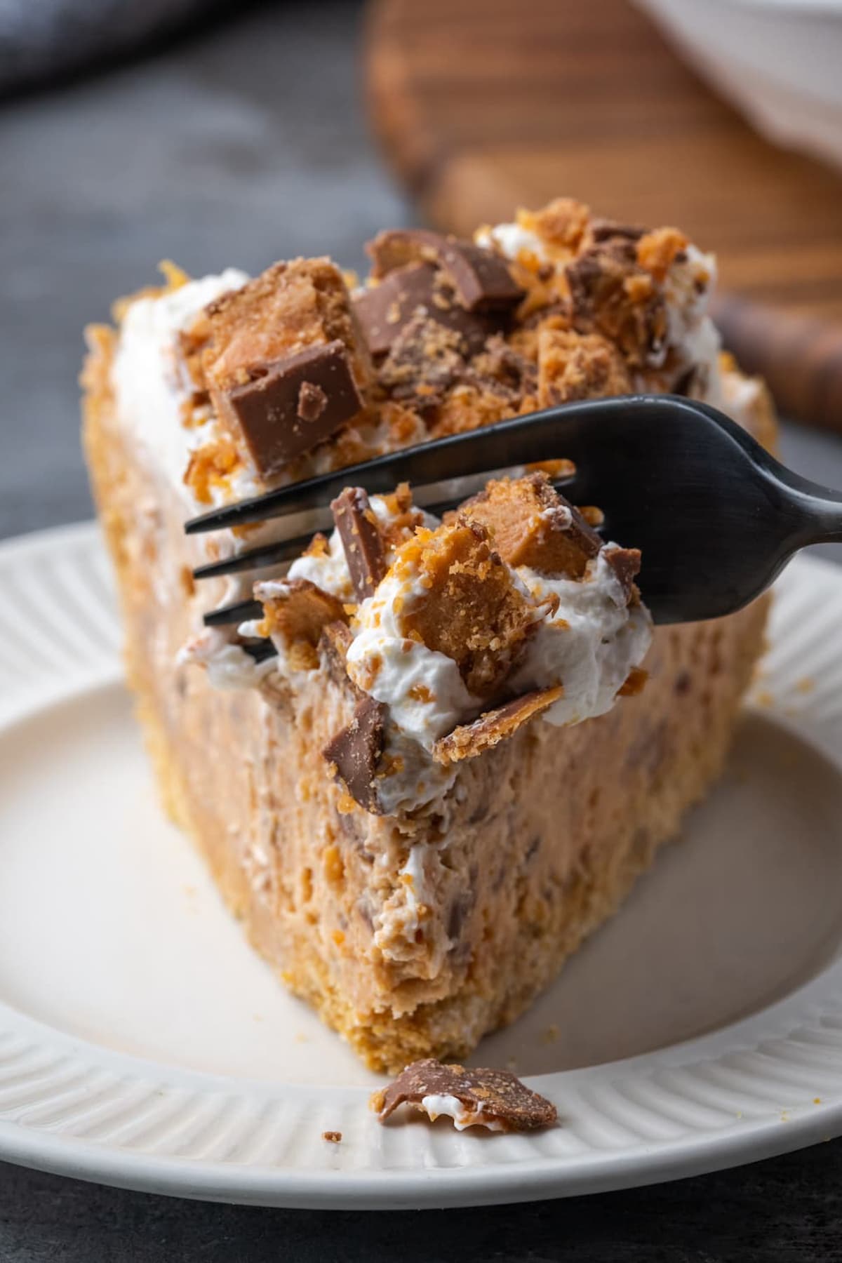 A fork cuts into a slice of Butterfinger pie on a white plate.