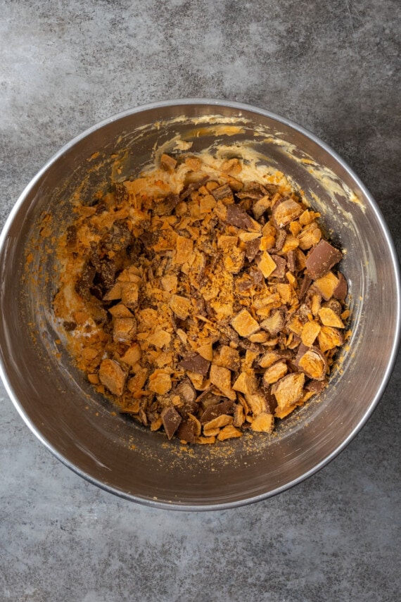 Chopped Butterfinger candy is added into a bowl of peanut butter mixture for the pie filling.