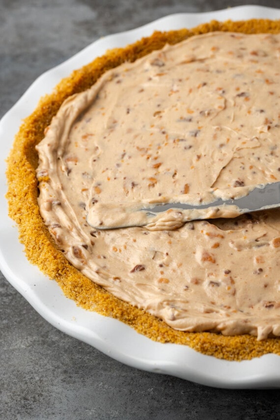 Butterfinger pie filling is spread into a pie crust with an offset spatula.
