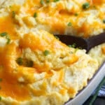 Cheese topped baked mashed potatoes with a wooden spoon to serve