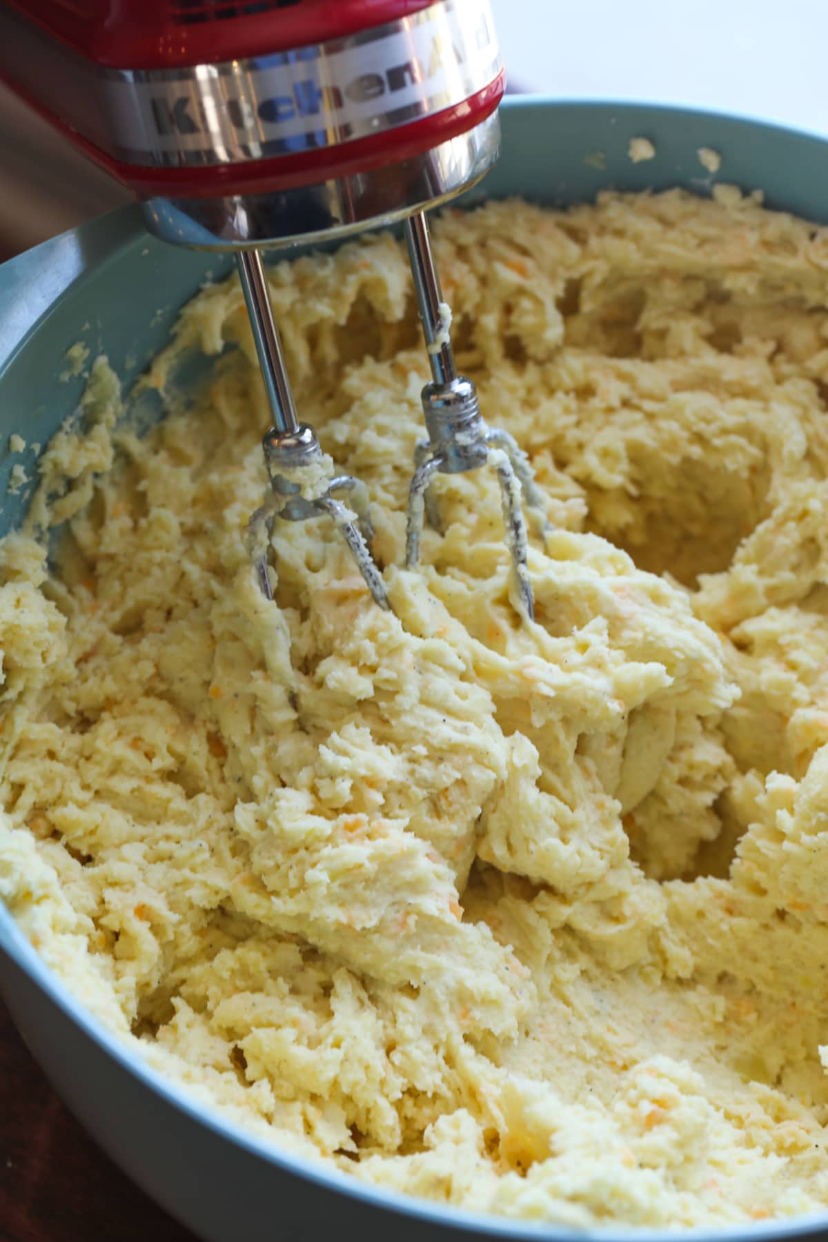 mashing potatoes in a blue mixing bowl with an electric hand mixer