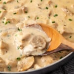 Close up of cream of mushroom chicken in a skillet with a wooden spoon.