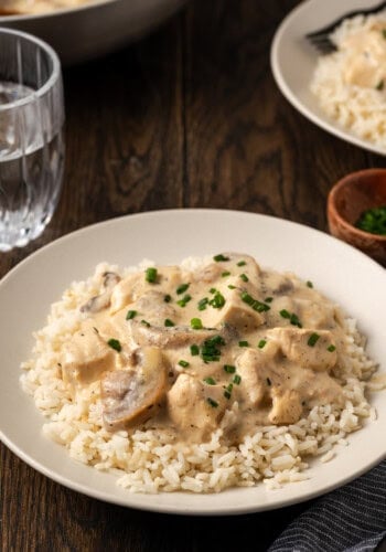 A bowl of cream of mushroom chicken served over rice next to a glass of water.