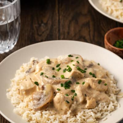 A bowl of cream of mushroom chicken served over rice next to a glass of water.