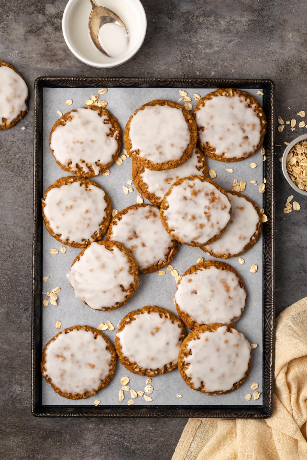 Overhead view of assorted iced oatmeal cookies scattered on a lined baking sheet.