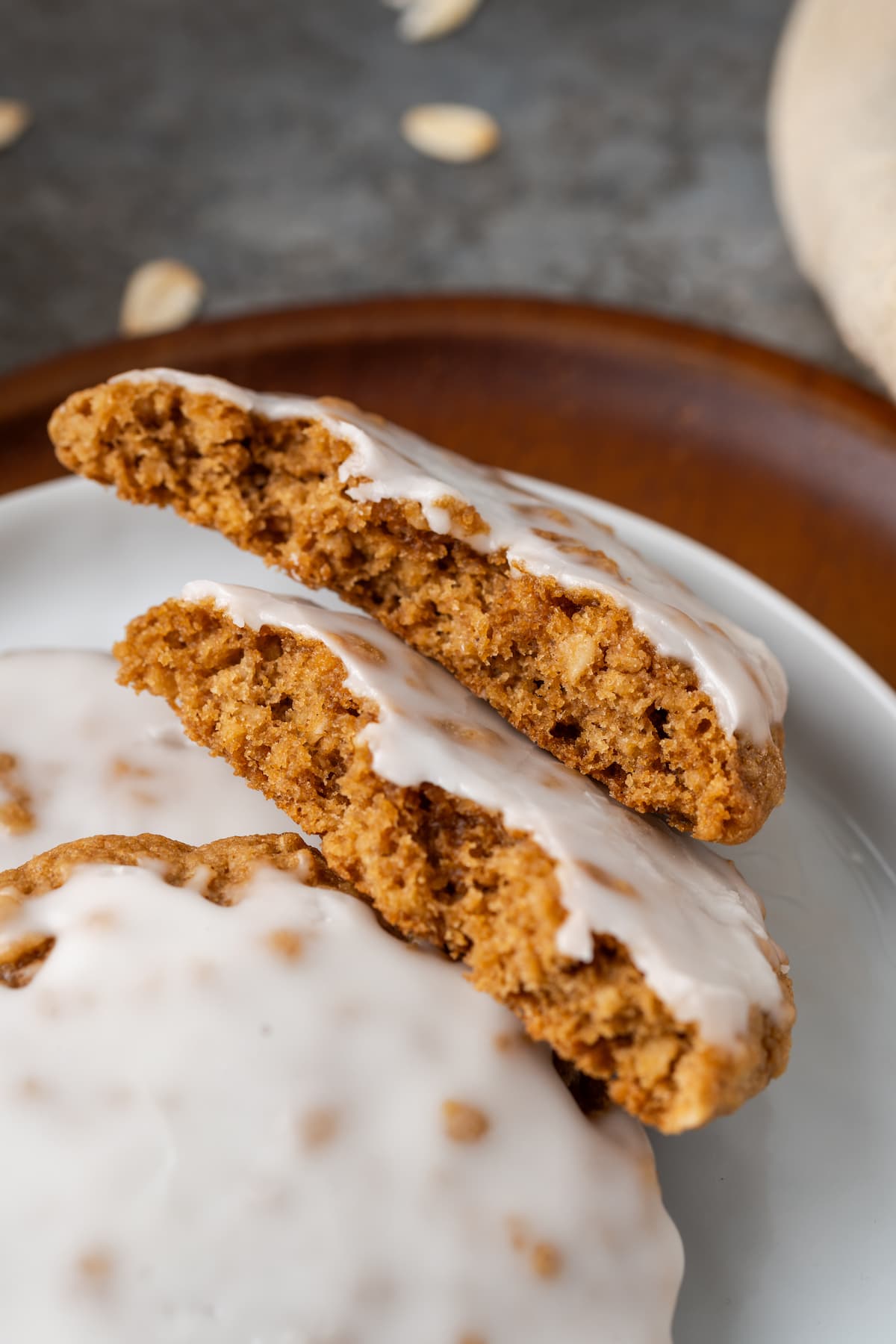 Close up of an iced oatmeal cookie broken in half, leaning against a stack of cookies on a plate.