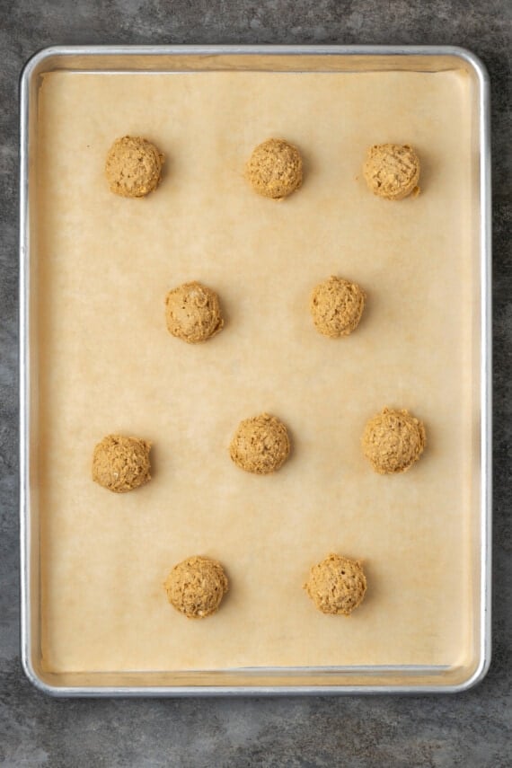 Oatmeal cookie dough balls arranged on a parchment-lined baking sheet.