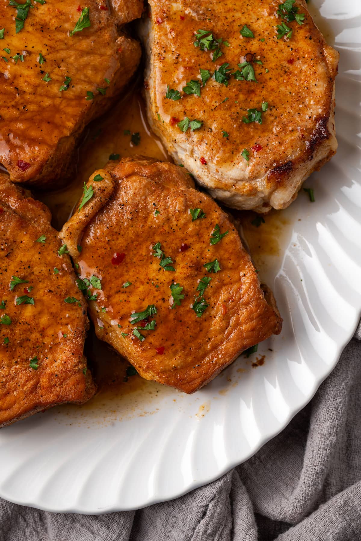 Overhead view of instant pot pork chops on a white platter garnished with fresh parsley.