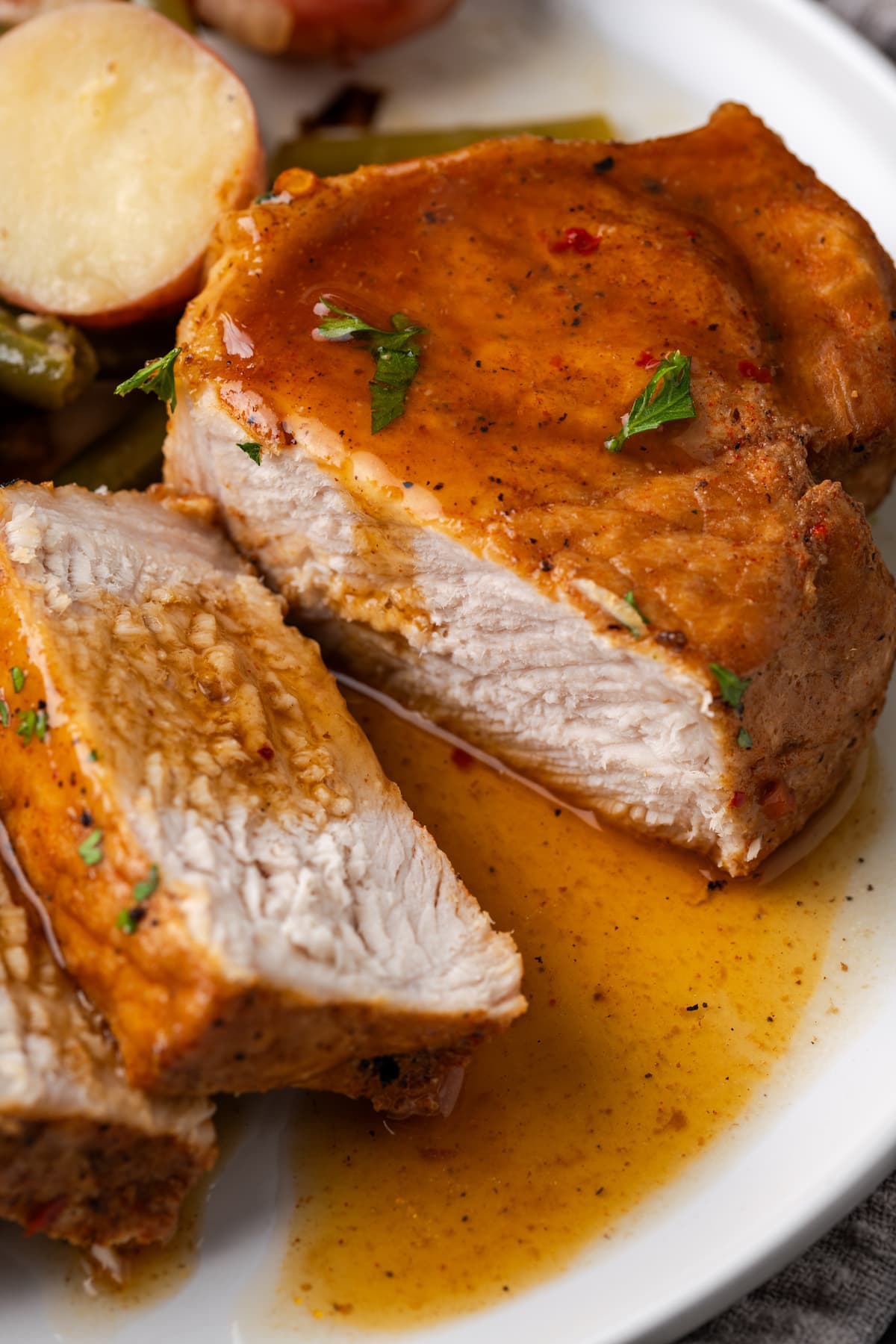 Close up of a pork chop cut into slices next to green beans and baby red potatoes on a white plate.