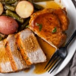 Overhead view of a pork chop cut into slices next to green beans and baby red potatoes on a white plate.