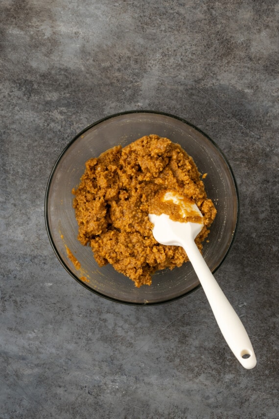 Graham cracker crust mixture in a glass bowl with a rubber spatula.