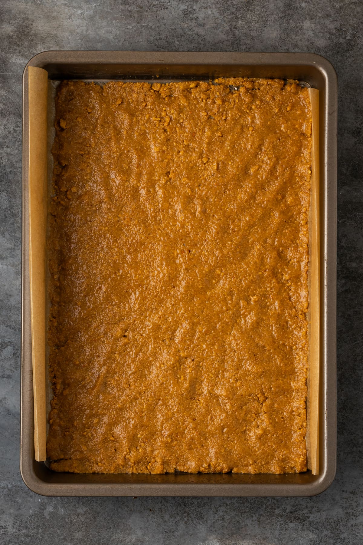 A layer of graham cracker crumbs in a lined baking pan.