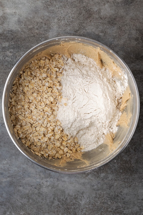 Oats and dry ingredients added to creamed butter and sugar in a mixing bowl.