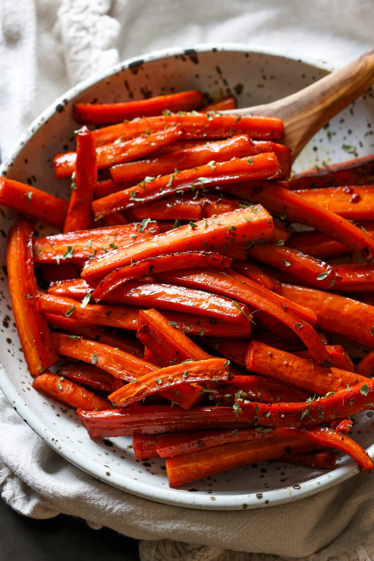 Roasted carrots in a serving bowl with a wooden serving spoon