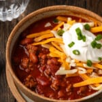 Instant pot chili garnished with shredded cheese, sour cream, and chives in a stoneware bowl.