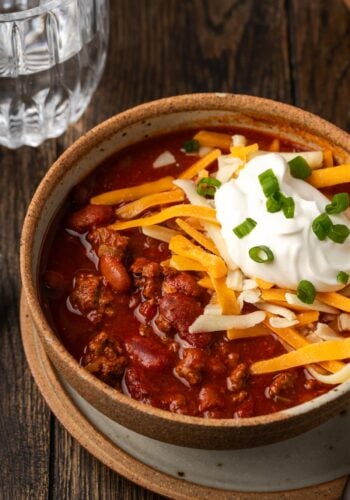 Instant pot chili garnished with shredded cheese, sour cream, and chives in a stoneware bowl.