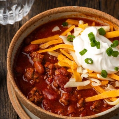 Instant pot chili garnished with shredded cheese, sour cream, and chives in a stoneware bowl.